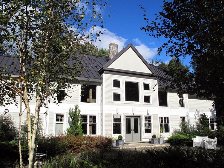 A large white house with a black roof is surrounded by trees