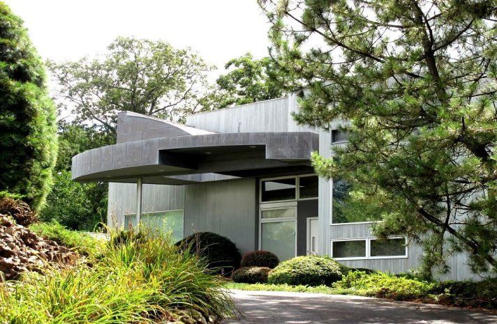 A house with a curved roof is surrounded by trees and bushes
