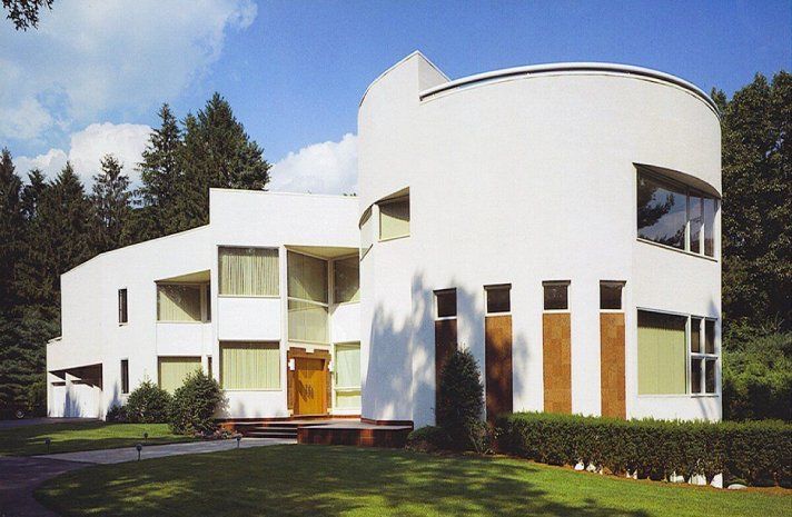 A large white house with a curved roof is surrounded by trees