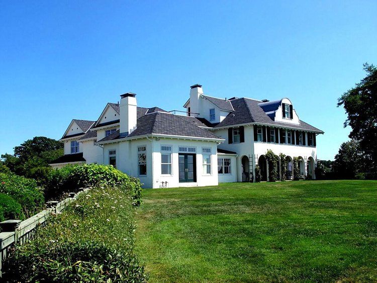 A large white house sits in the middle of a lush green field