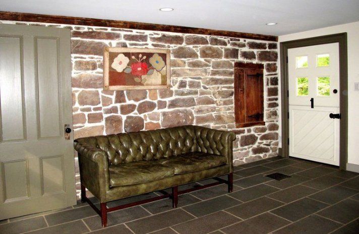 A green leather couch is sitting in front of a stone wall.