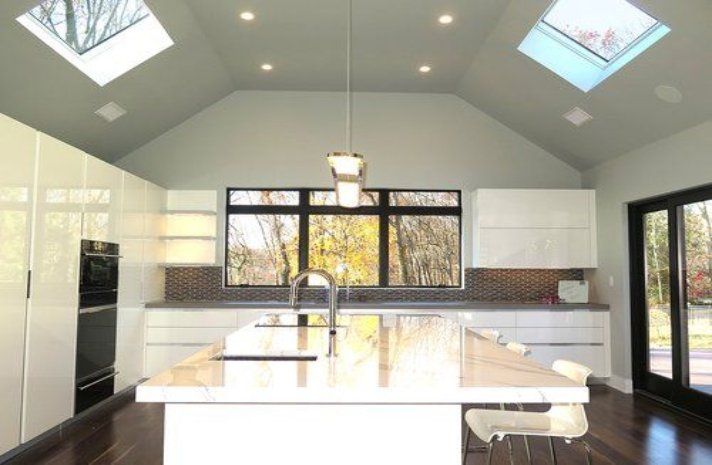 A kitchen with white cabinets , a large island , a skylight and a vaulted ceiling.