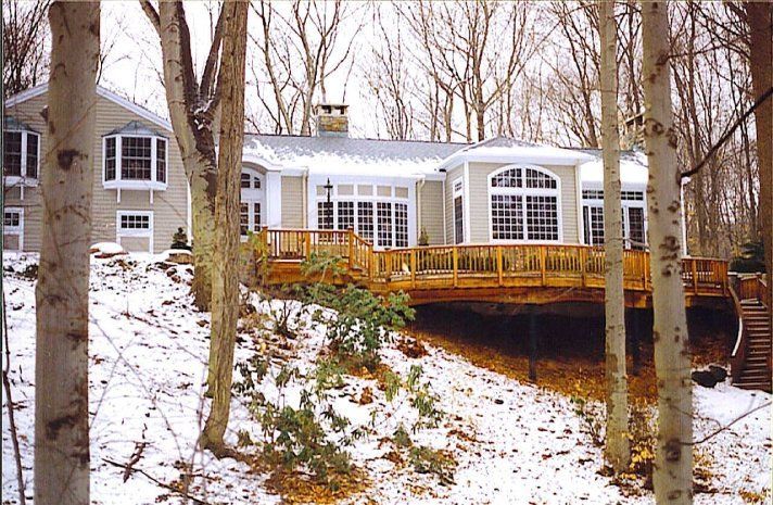 A house with a large deck is surrounded by snow covered trees