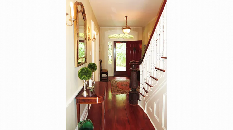 A hallway with a staircase and a mirror on the wall.