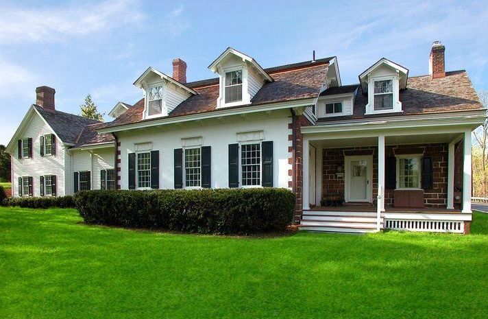 A large white house with black shutters is sitting on top of a lush green lawn.