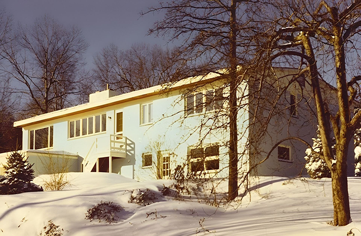 A white house is surrounded by snow and trees