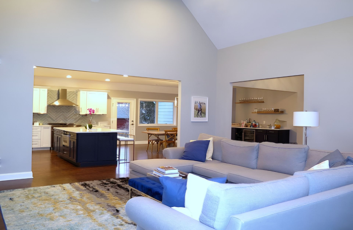 A living room with a couch and a rug and a kitchen in the background.