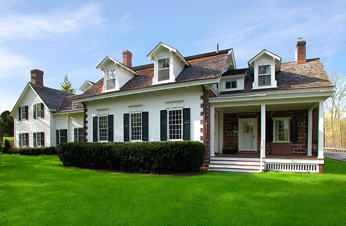 A large white house with black shutters sits on a lush green lawn