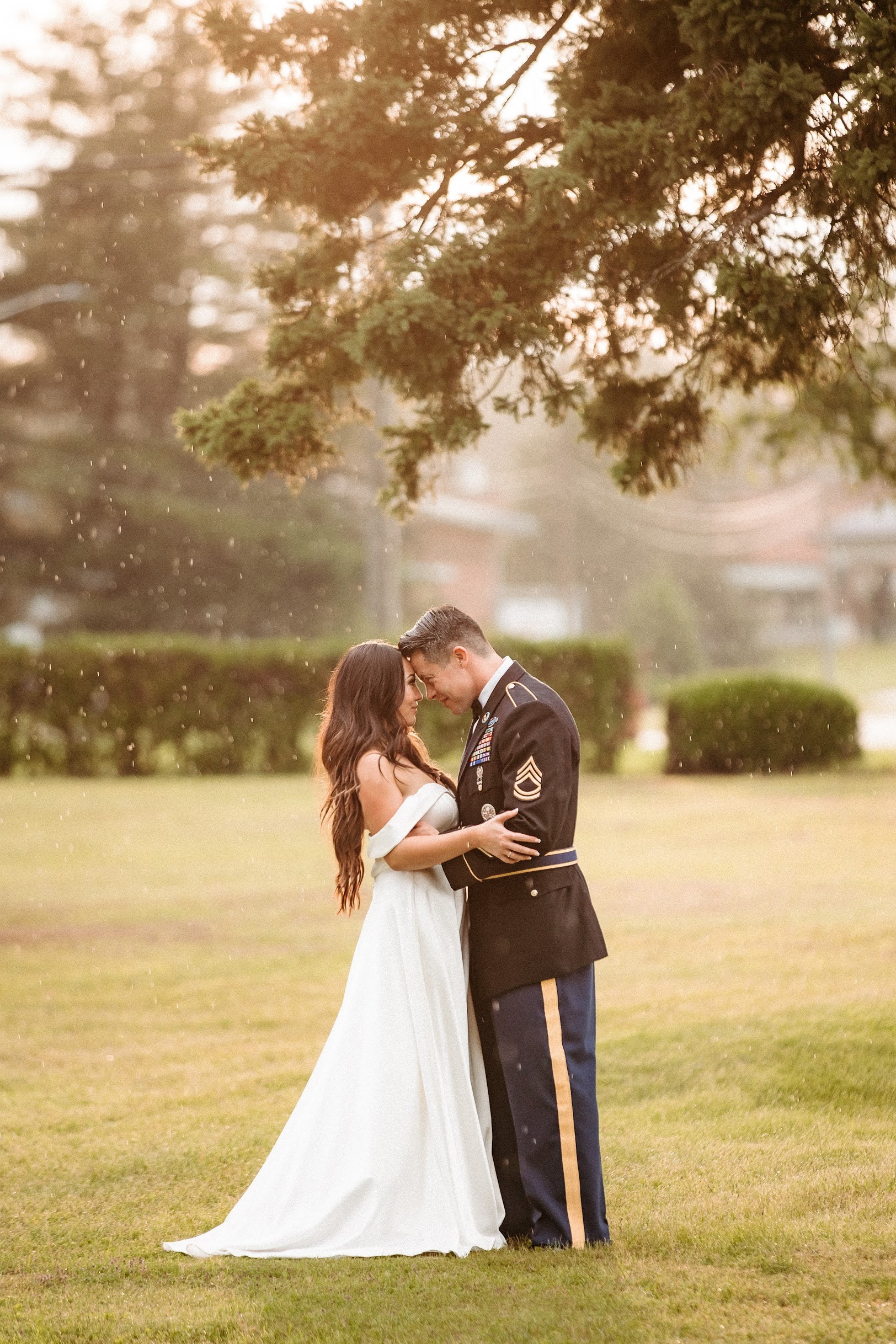 A bride and groom are kissing under a tree in the rain on West Side's lawn.