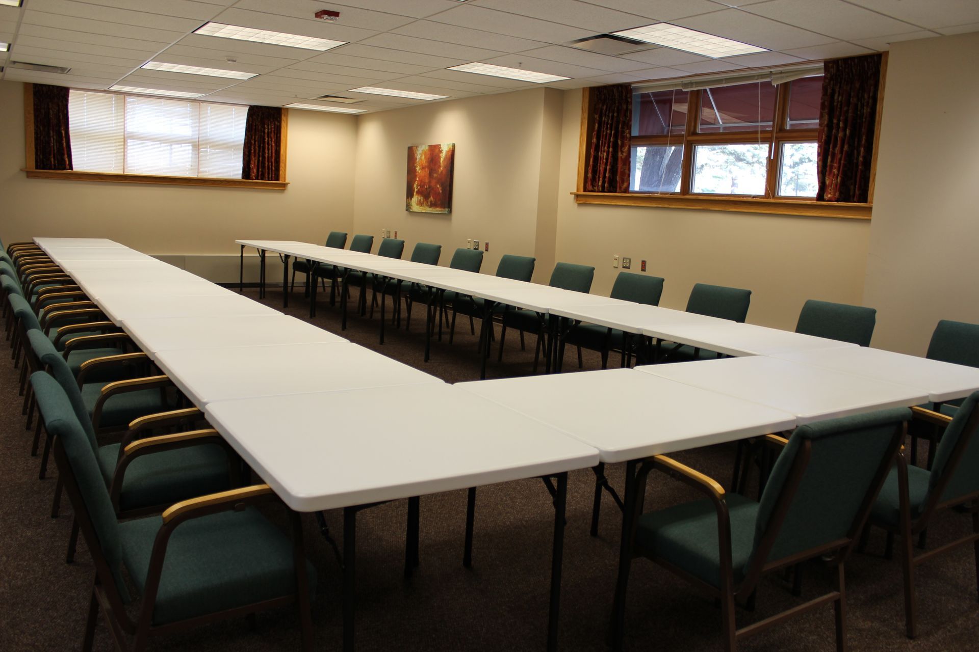 A conference room with long tables and green chairs with room for 20 attendees.