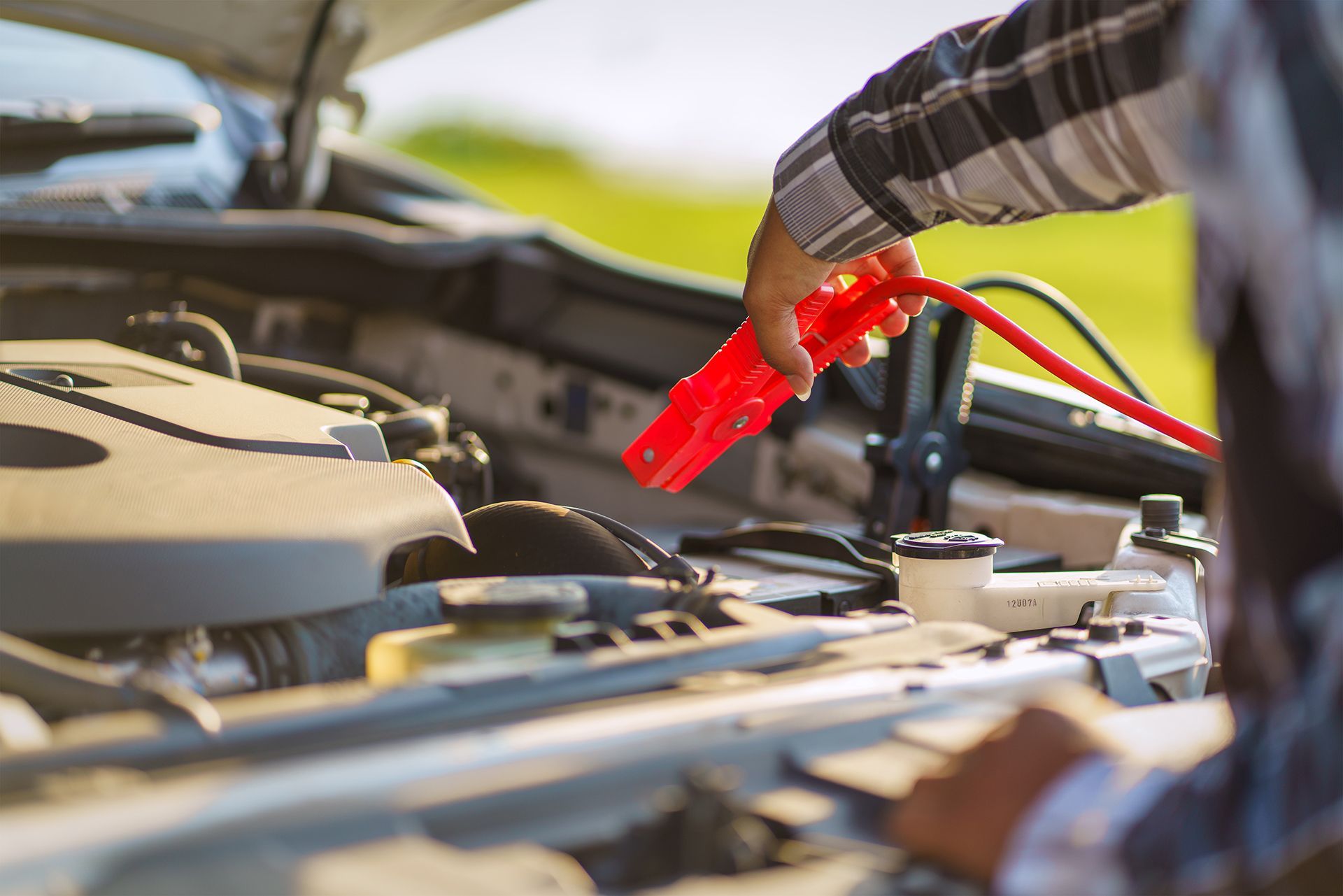 Un uomo sta caricando la batteria di un'auto con un caricabatterie rosso.