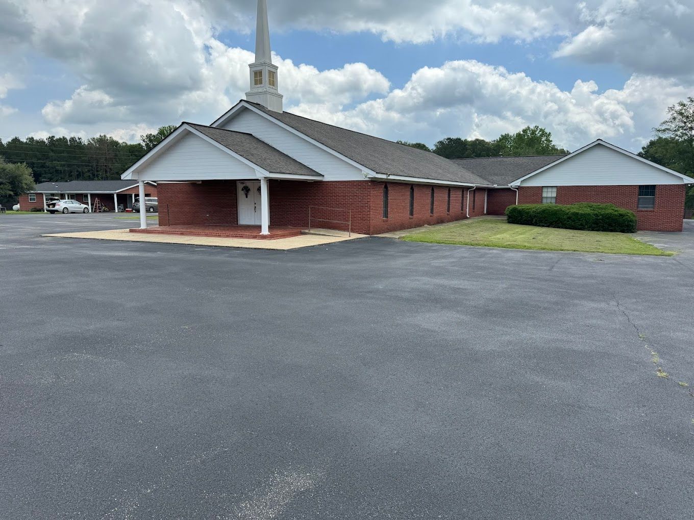 A church with a steeple and a parking lot in front of it