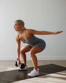 A woman is squatting on a yoga mat while holding a dumbbell. Forever Fit - Personalised Workouts and Nutrition