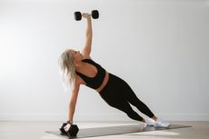 A woman is doing a plank exercise with a dumbbell over her head. Forever Fit - Personalised Workouts and Nutrition