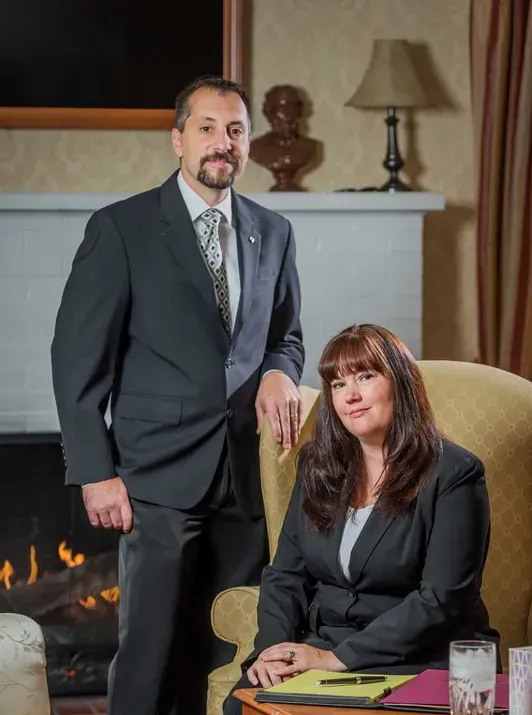 Daniel Bitecola standing in front of a fireplace next to Melanie Bitecola sitting in a chair.