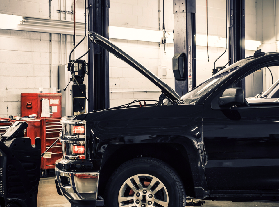Black pickup truck in a garage with its hood open, near tools and equipment.