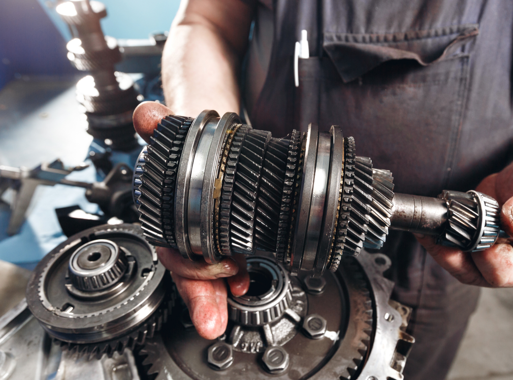 Mechanic holding a metal transmission gear assembly in a workshop