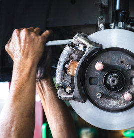 Hands using a wrench to repair a car’s brake rotor and caliper in a garage.