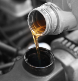 Motor oil pouring from a bottle into an engine fill cap, with the scene in grayscale and amber oil highlighted