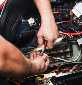 Hands using pliers to work on car wiring and fuse box under the dashboard