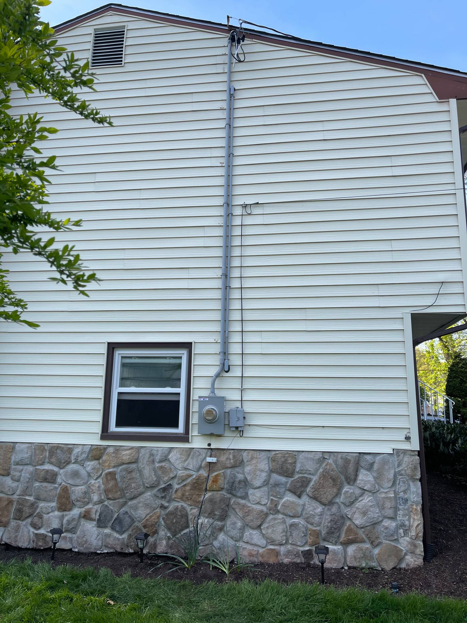 Exterior wall of a house with white siding, electrical conduit, meter, window, and stone base.