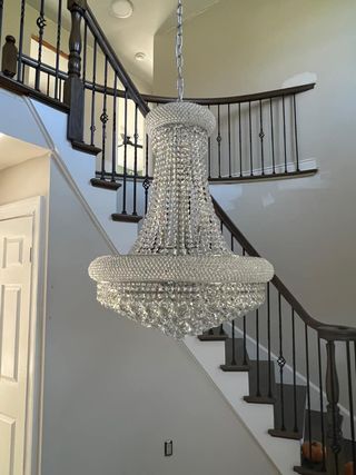 Large crystal chandelier hanging in a stairwell. Stairs have dark wood banister and railings.