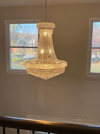 Crystal chandelier hanging between two windows in a room with a light-colored wall.