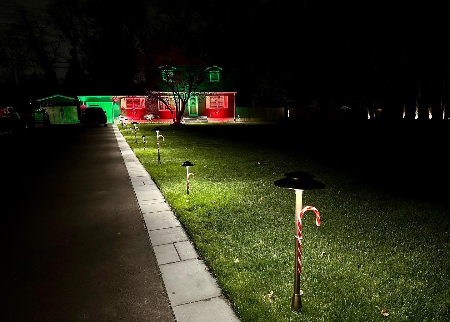 A house at night with Christmas lights. Green and red lights illuminate the home and lawn. Candy cane yard lights line the grass.