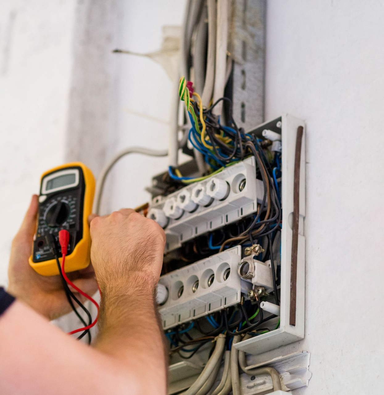 Electrician testing voltage on a fuse box, showcasing local electrical contractor expertise.