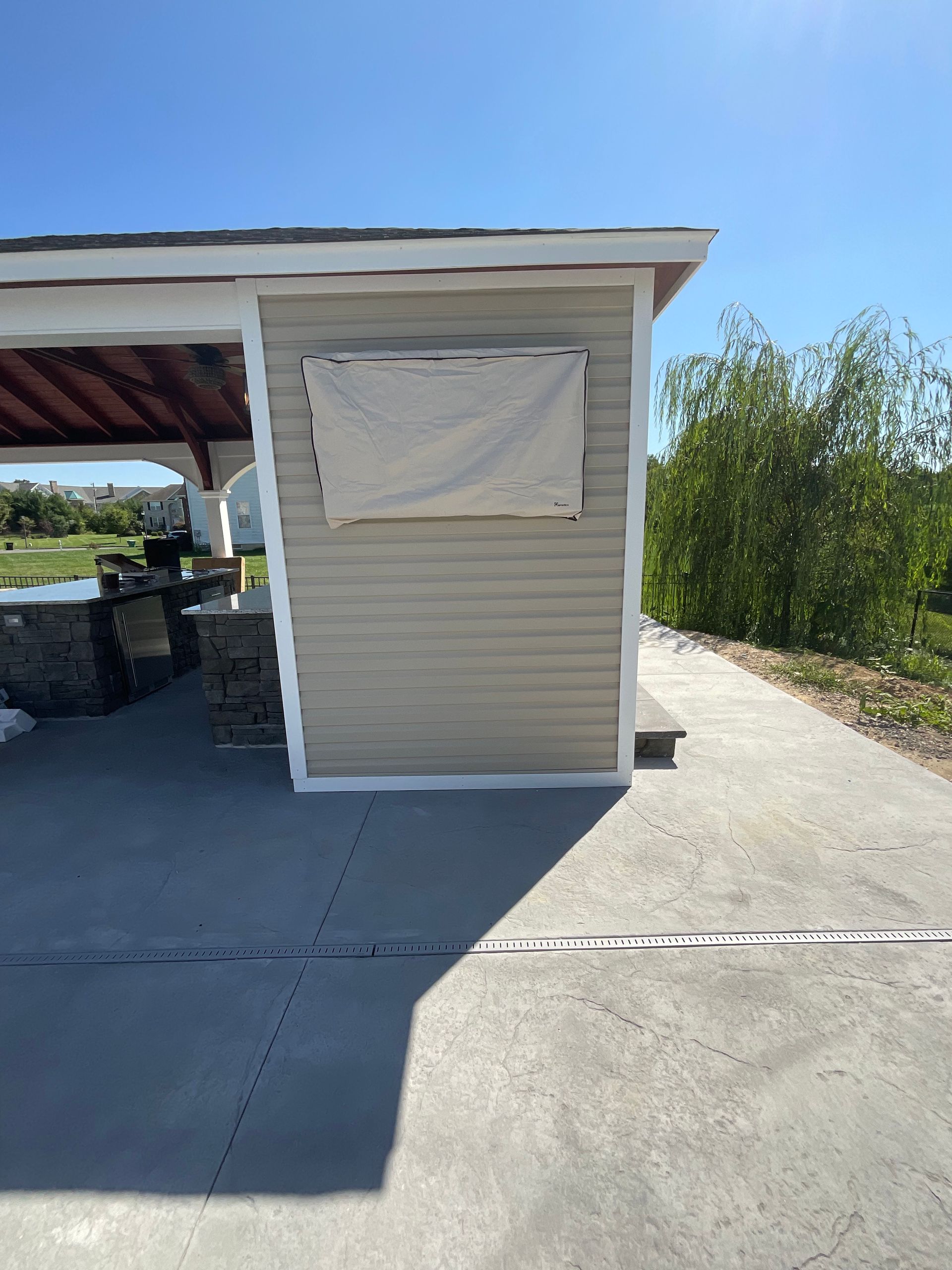 Outdoor structure with tan siding, covered window, and concrete patio.