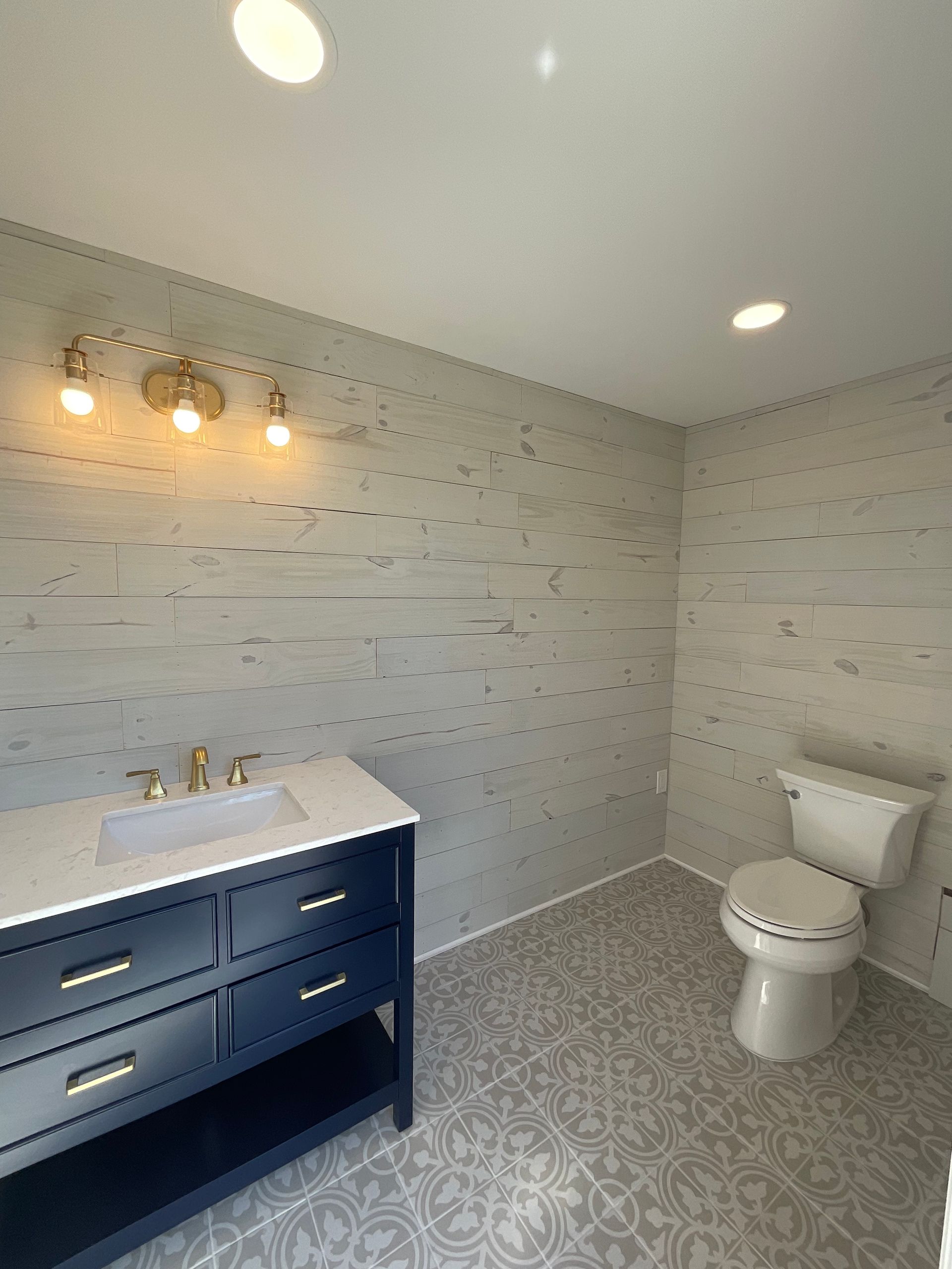 Bathroom with blue vanity, white countertop, gold fixtures, and gray and white plank-style tile.