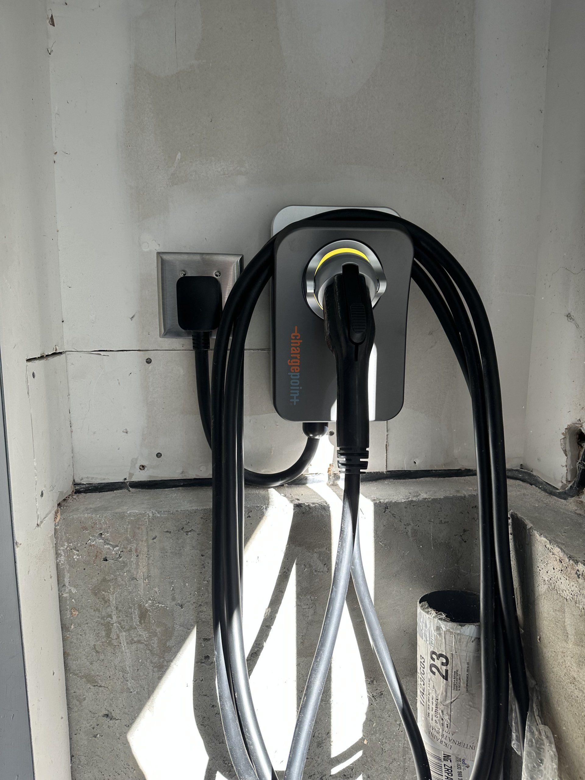 Electric vehicle charger mounted on a concrete wall; black and white charging cables and outlet.