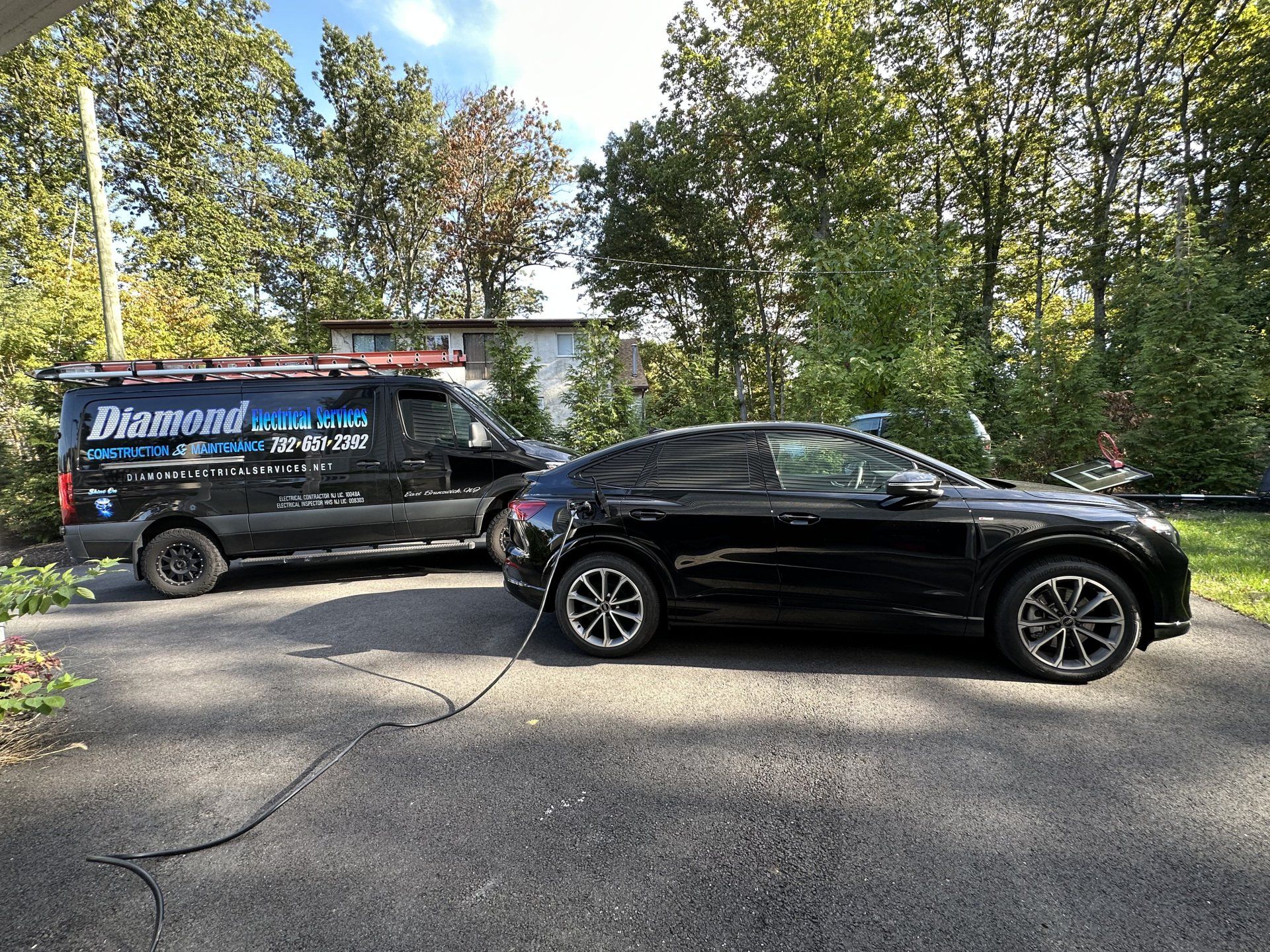 Black van and car connected by a cable, parked on a driveway in front of trees. 