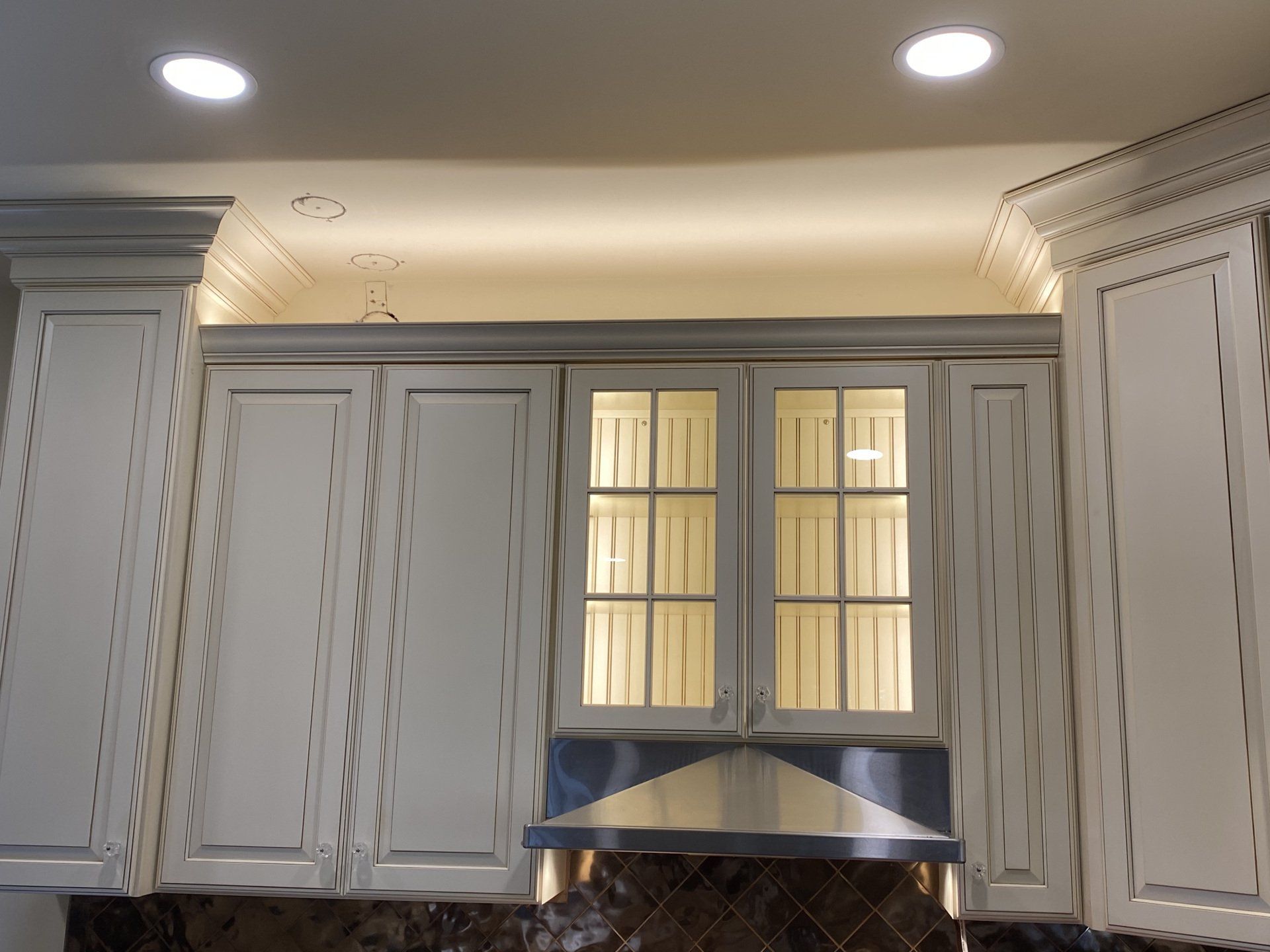 Cream-colored kitchen cabinets with accent lighting and a range hood.