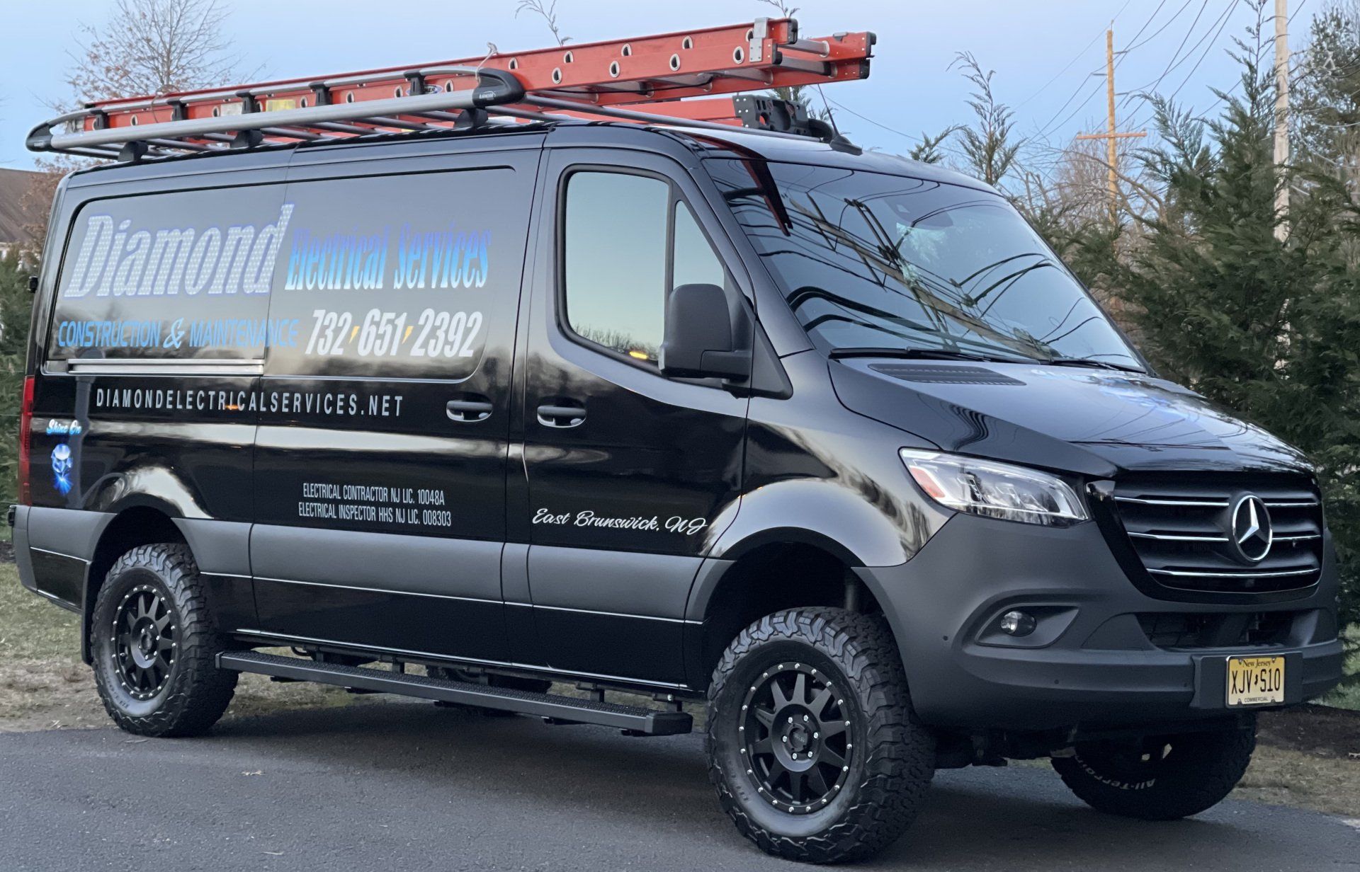 Black Diamond electric van with ladder on roof, parked on a street.