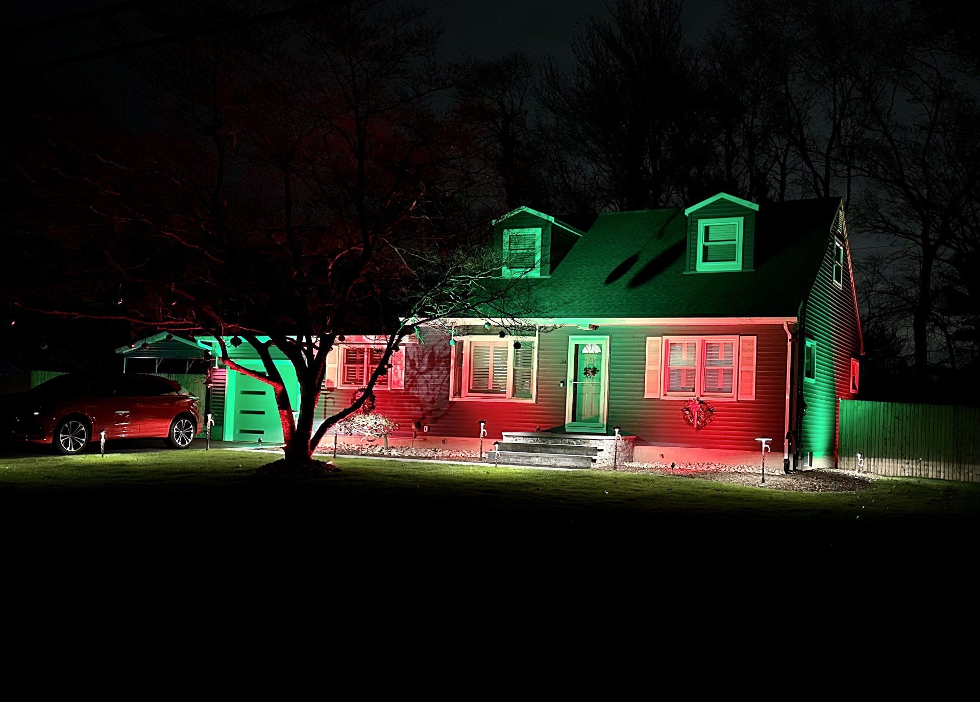 House with red and green Christmas lights, with a red car parked in the garage at night.
