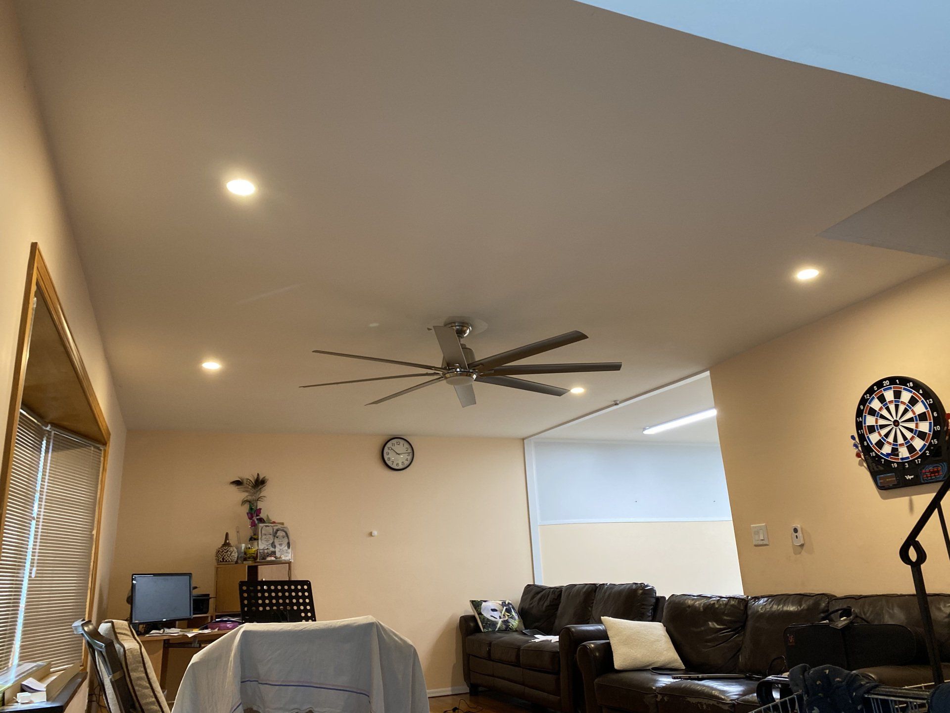 Living room with ceiling fan, recessed lights, and dartboard.
