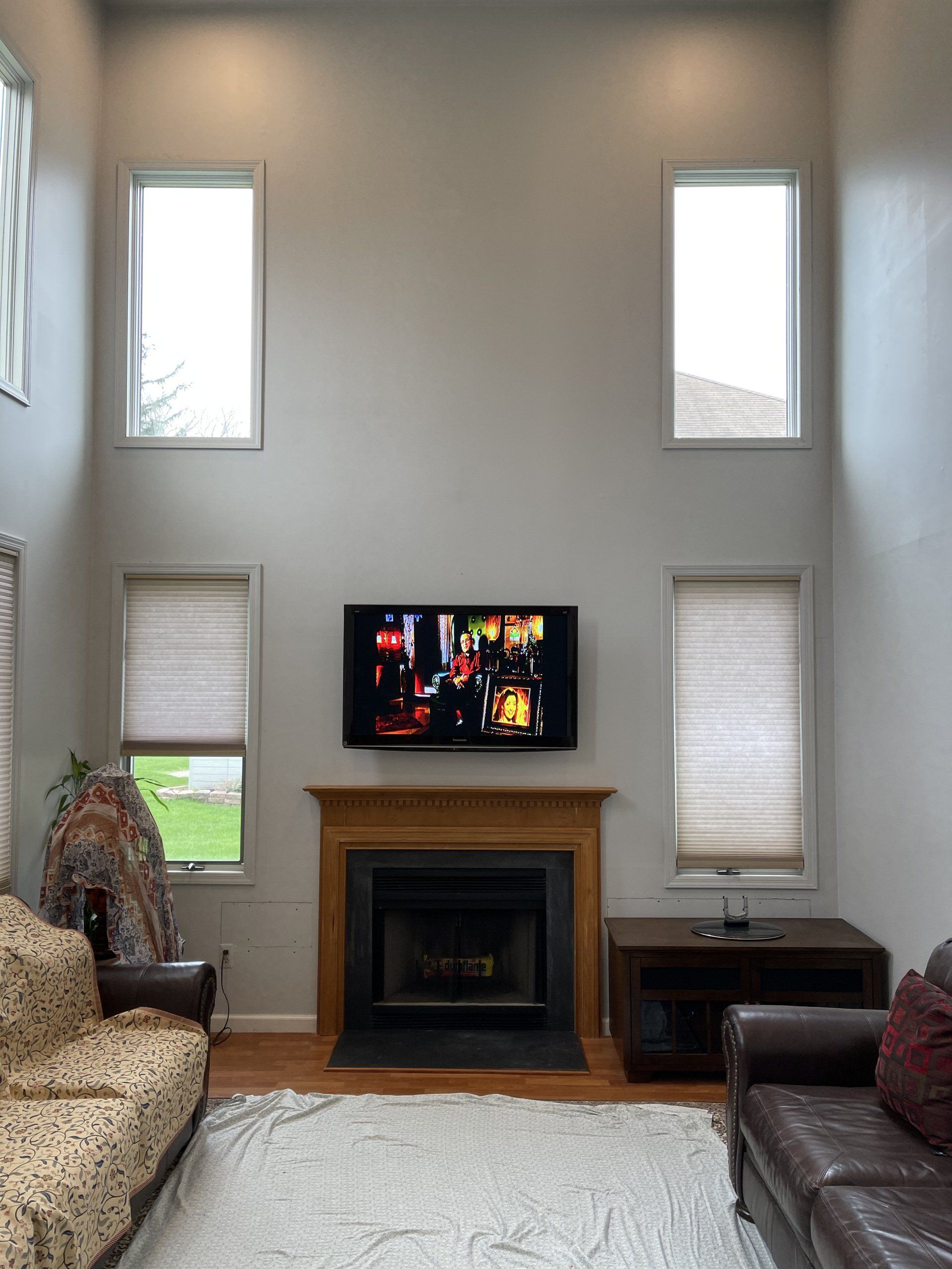 Living room with fireplace, TV, windows, sofa, and rug. Gray walls, light wood trim, and neutral colors.