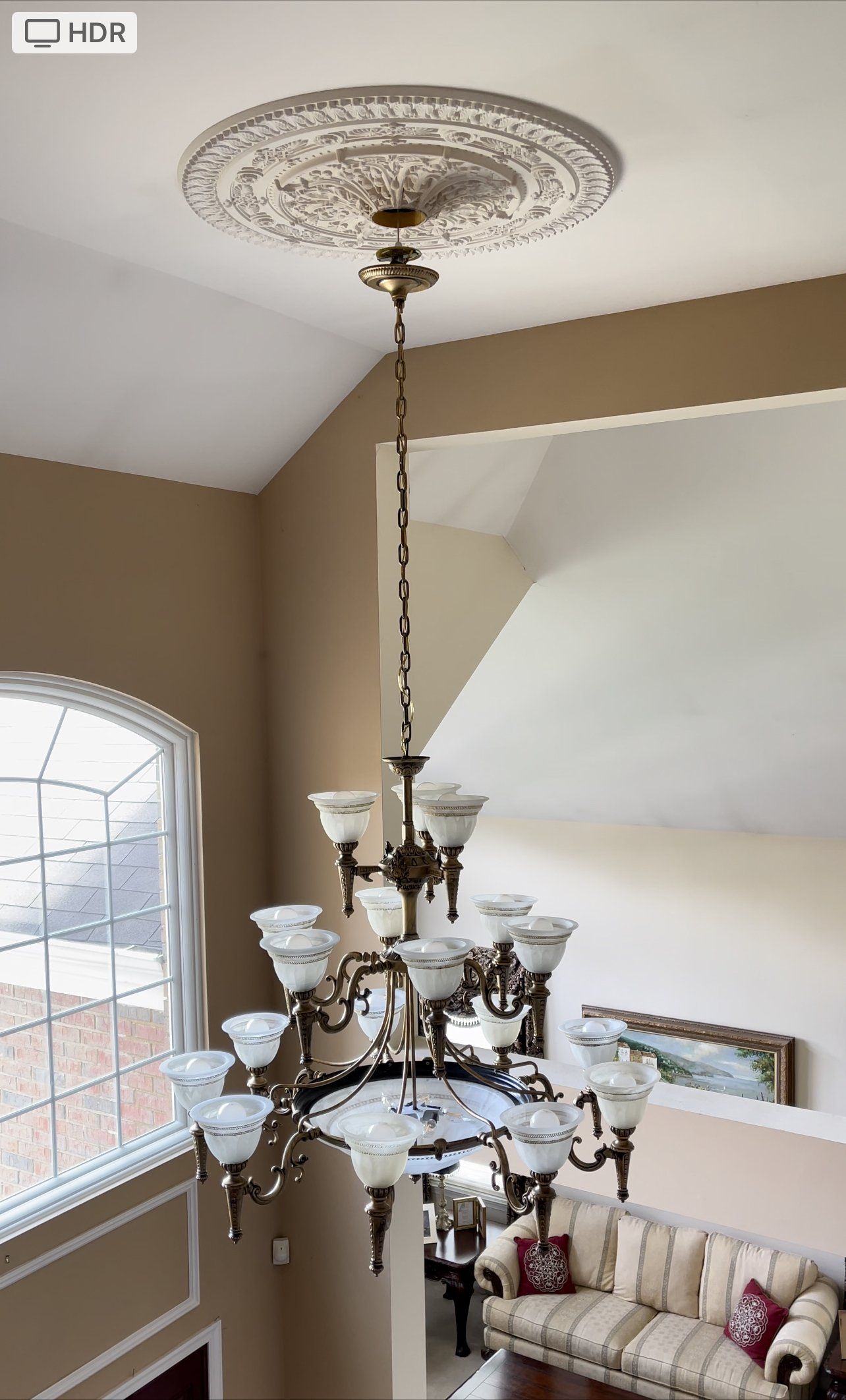 Chandelier hanging from ornate ceiling medallion in a two-story room, view from above.