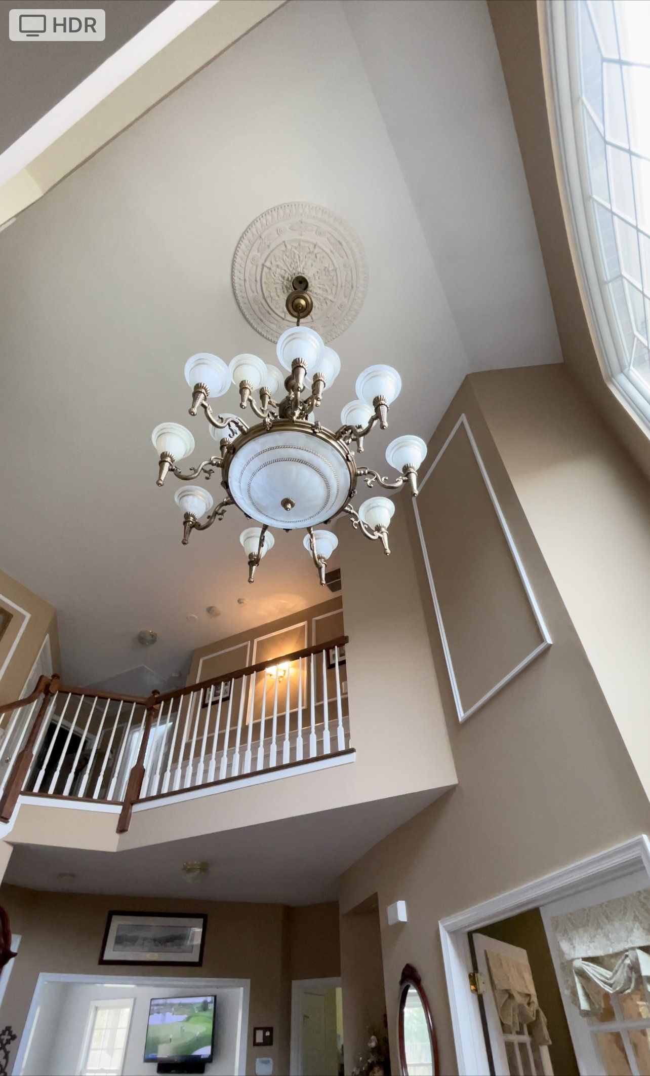 Chandelier hanging from a high ceiling in a home with a staircase.
