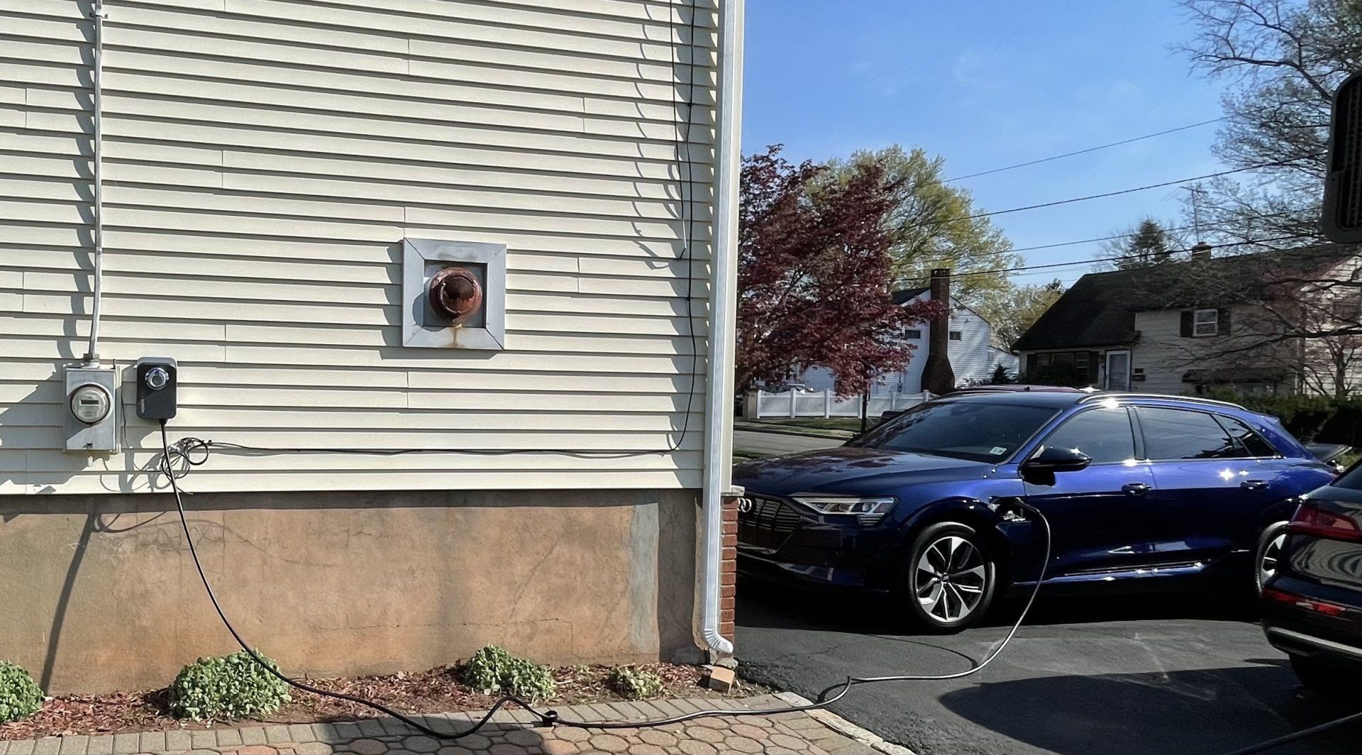 Blue electric car charging near a house, with a charging cable connected.