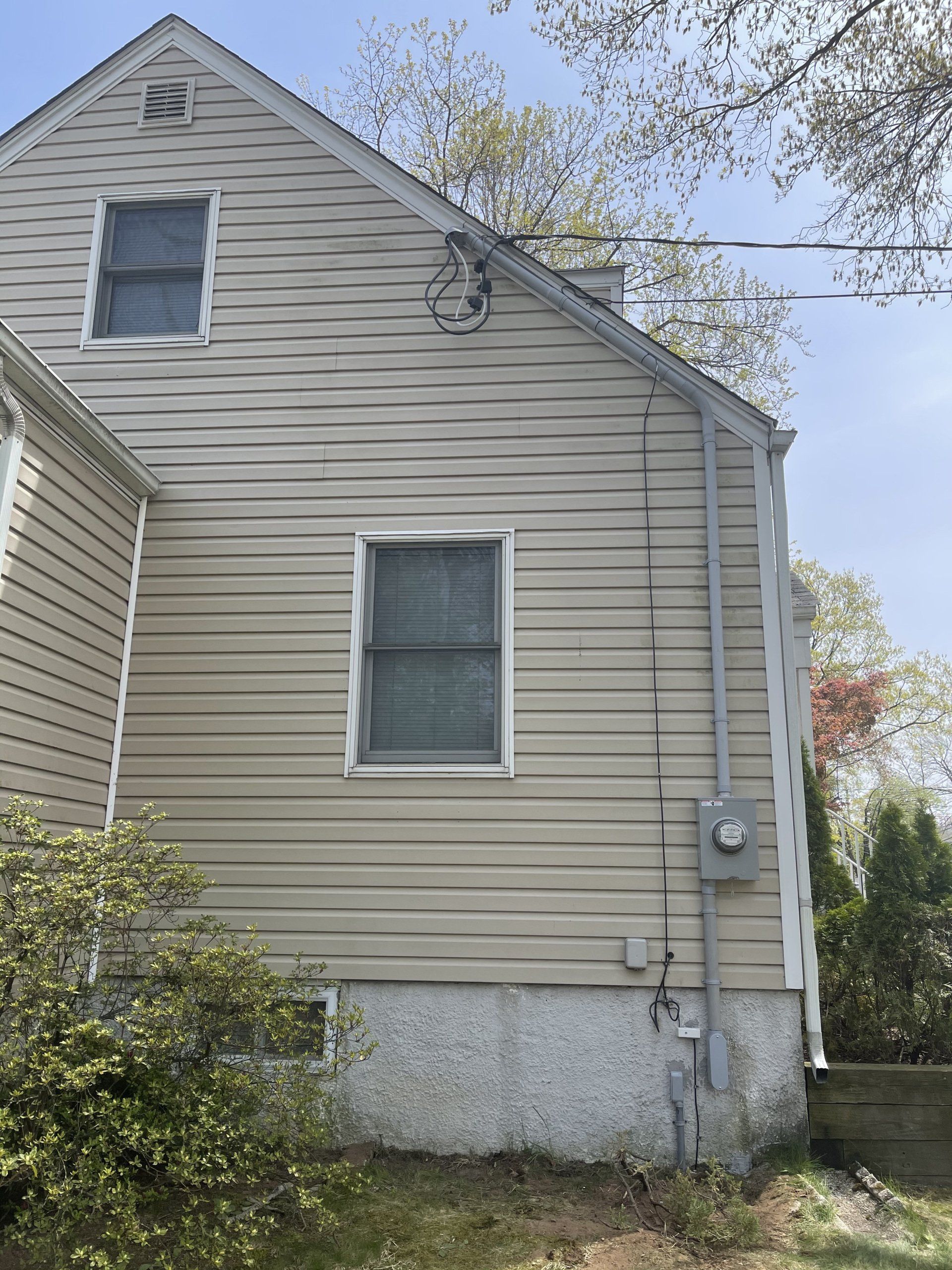 Side view of a house with beige siding, two windows, and electrical conduit running down the side.