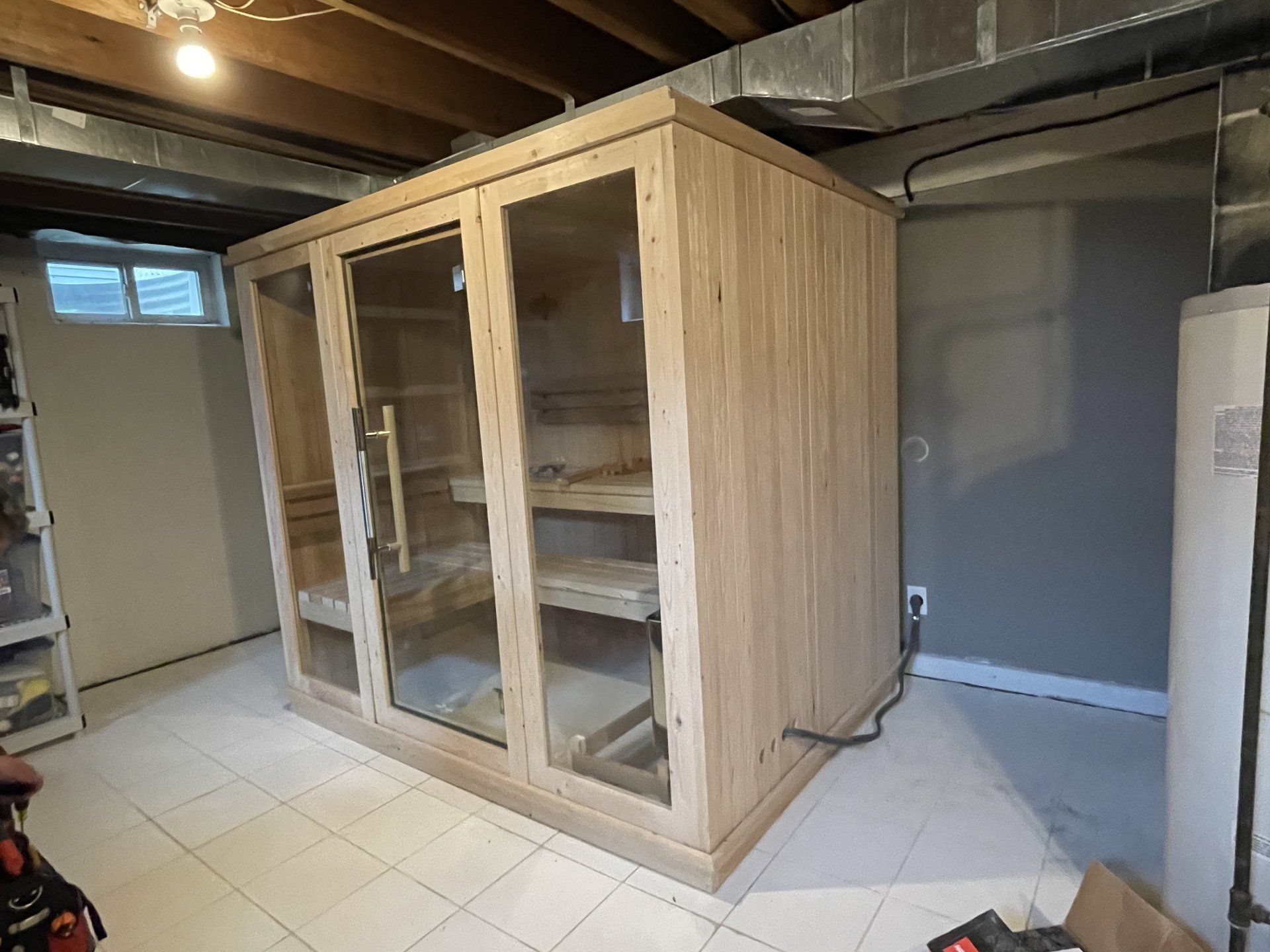 Light wood sauna with glass doors, built in a basement.