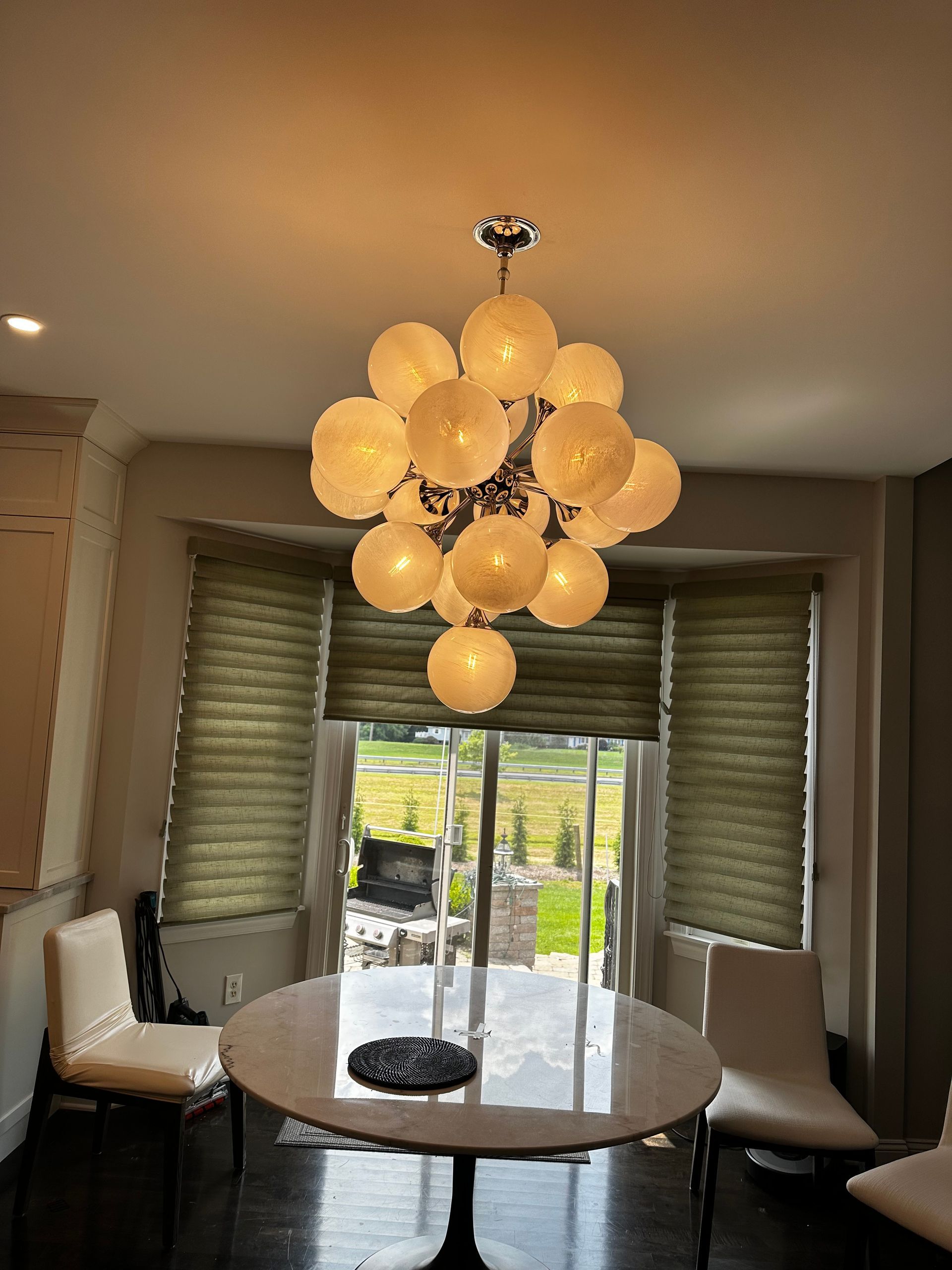 Dining room with round table, chairs, large chandelier, and window with outdoor view.