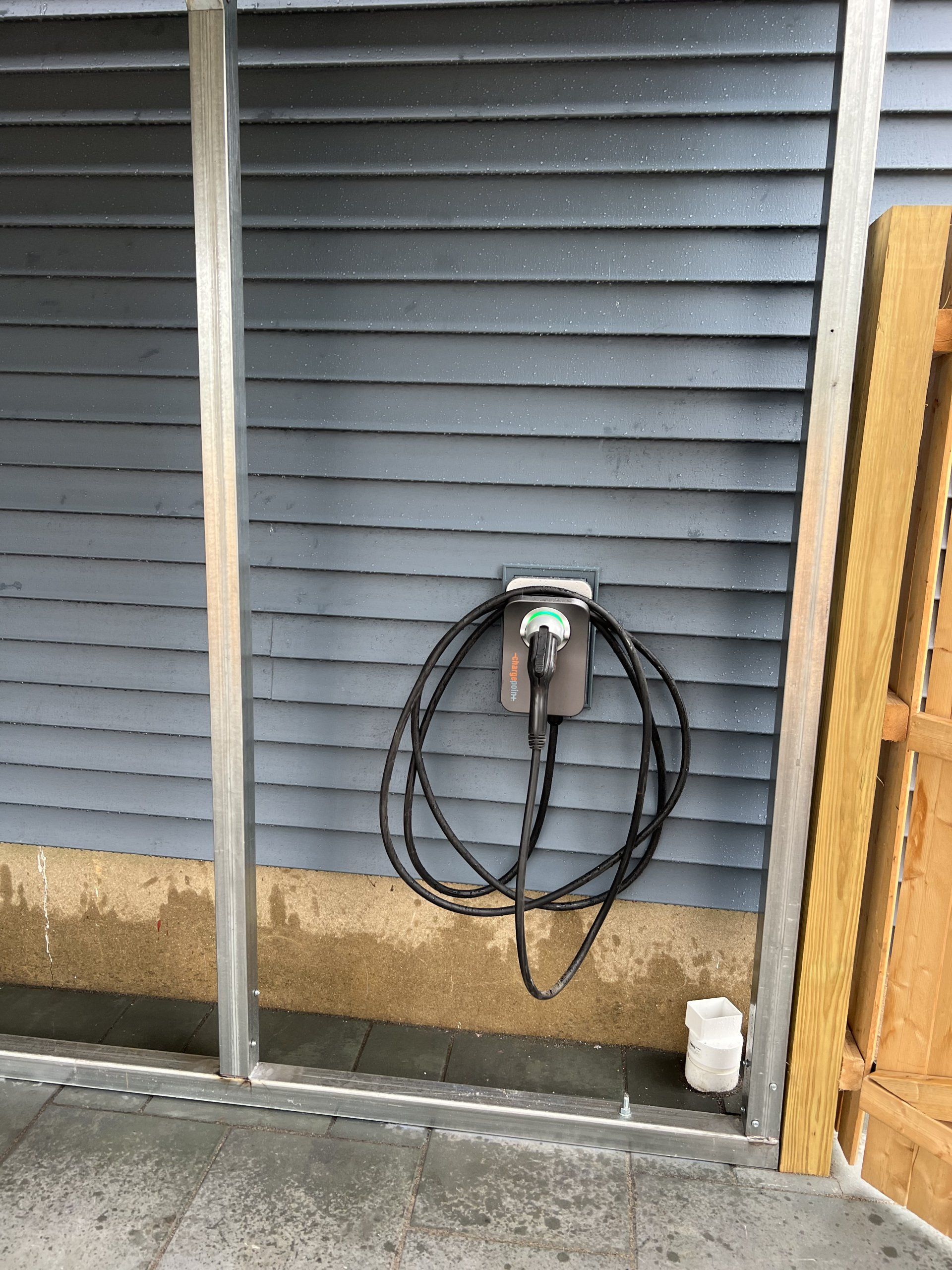 Electric vehicle charger on a gray wooden wall with a coiled black cable.