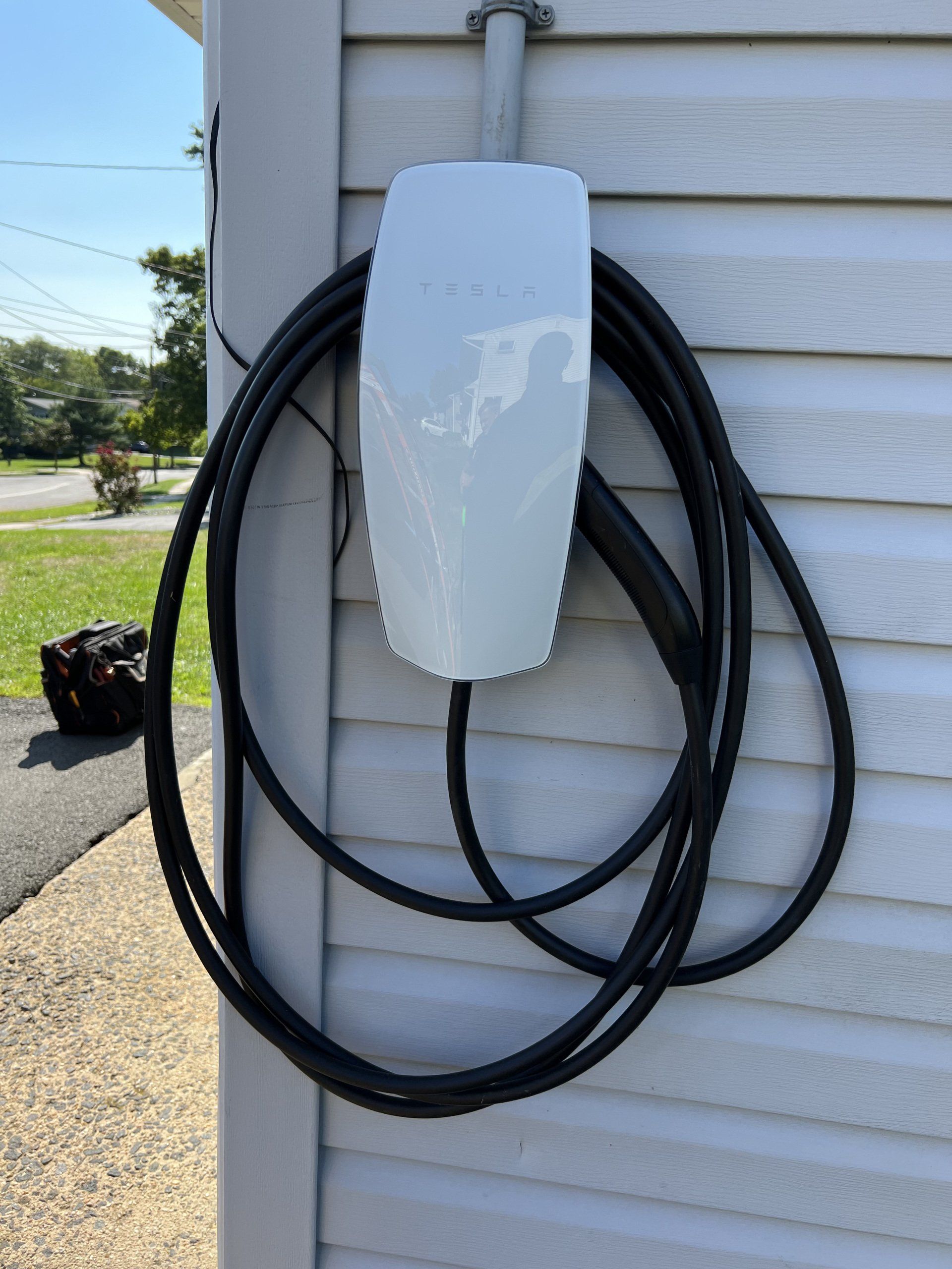Tesla electric vehicle charger mounted on a house exterior, with coiled black charging cable.