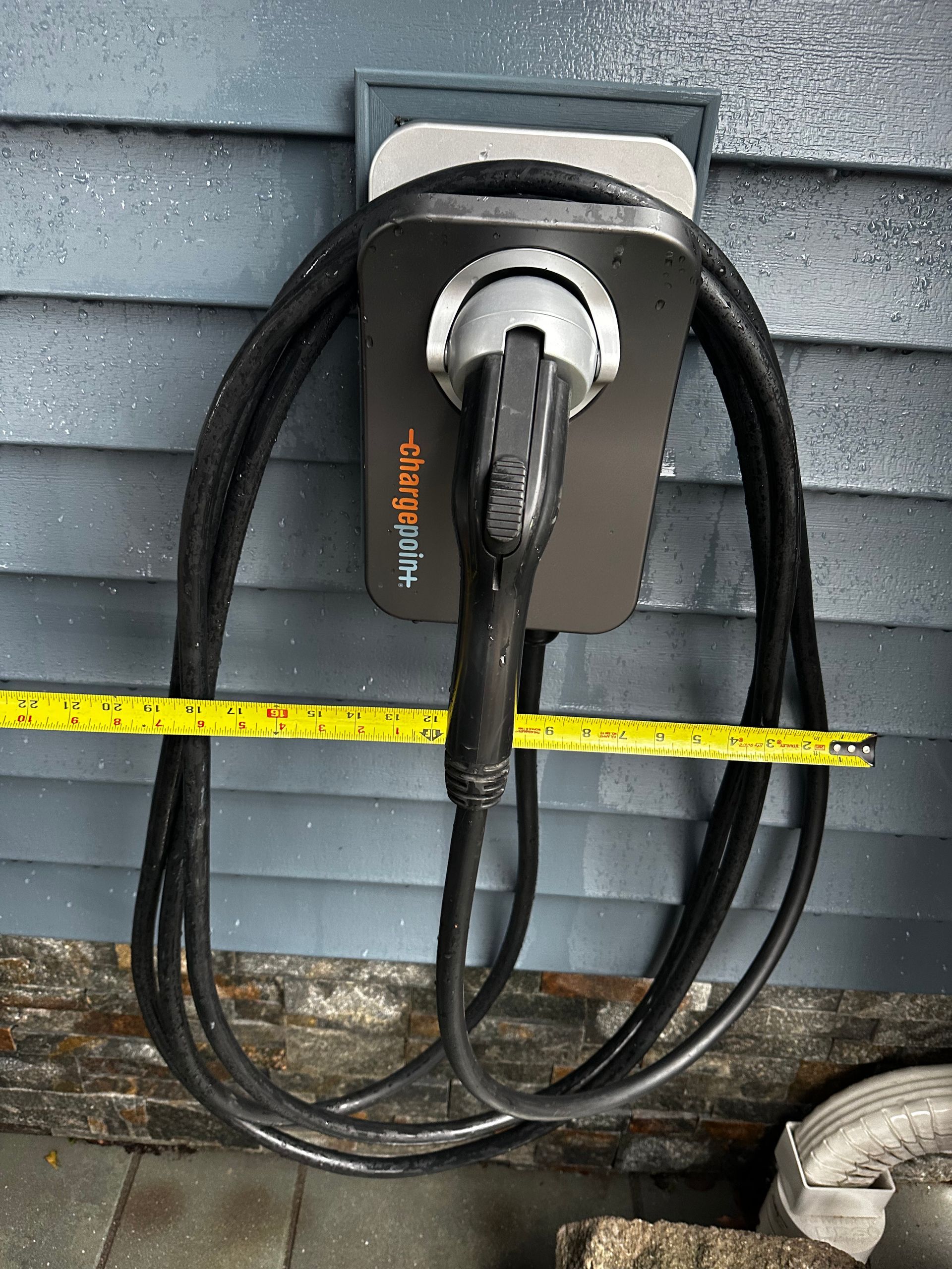 Black EV charger mounted on blue siding, yellow measuring tape below.