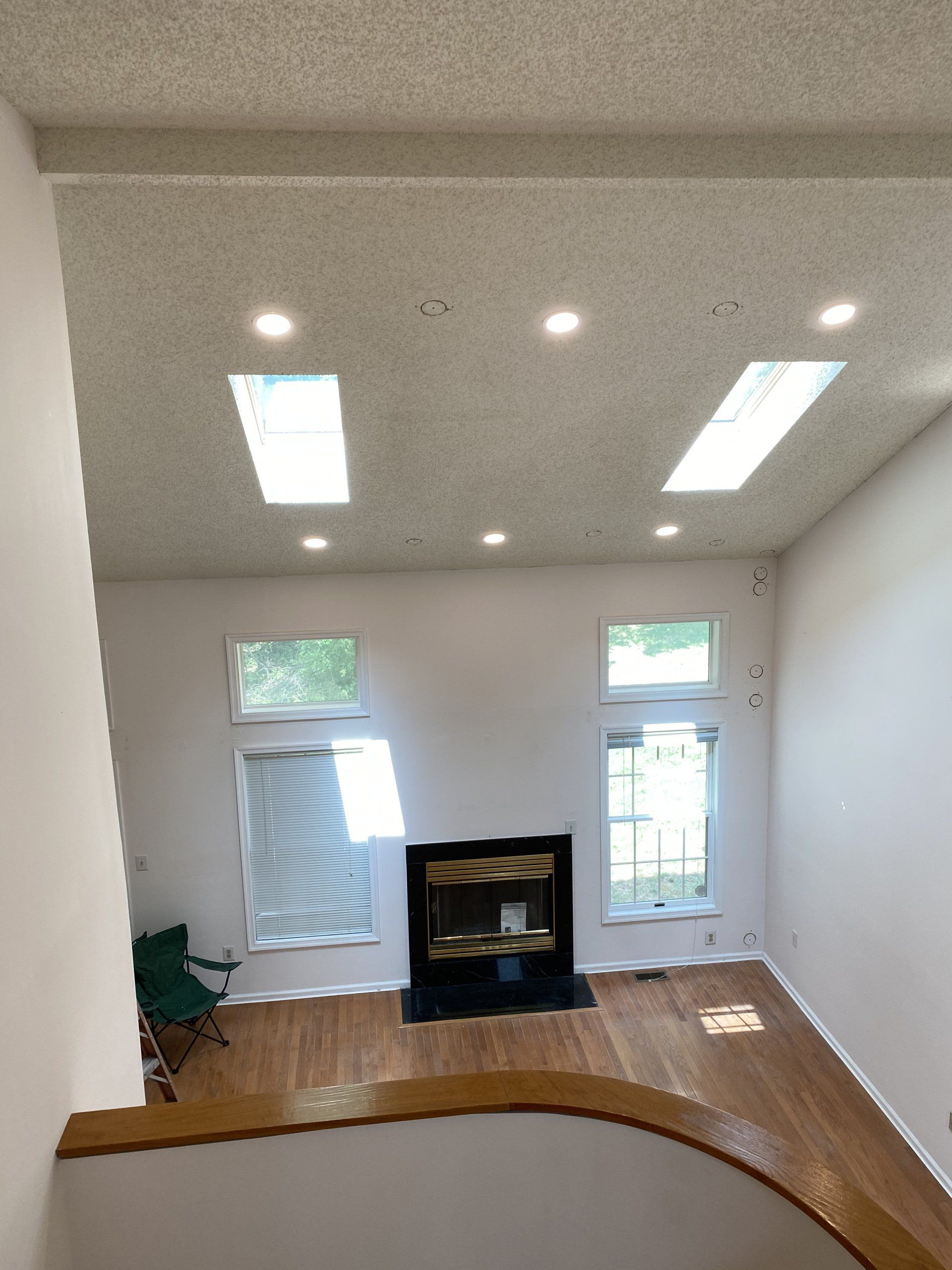 Interior view of a living room with a fireplace, skylights, and windows. Light wooden floor, white walls.