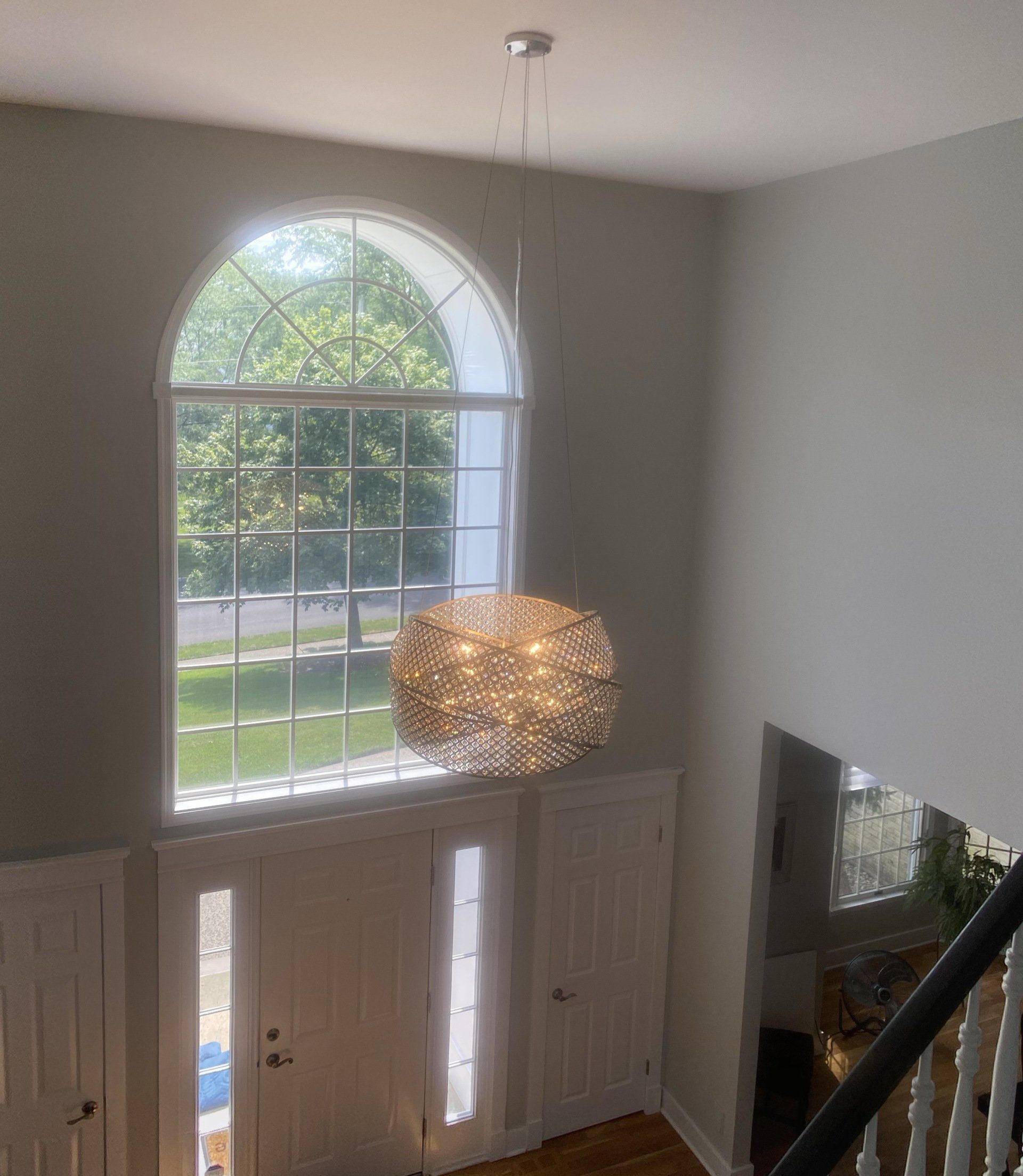 High angle view of entryway with large arched window, a decorative light fixture, and wooden floors.