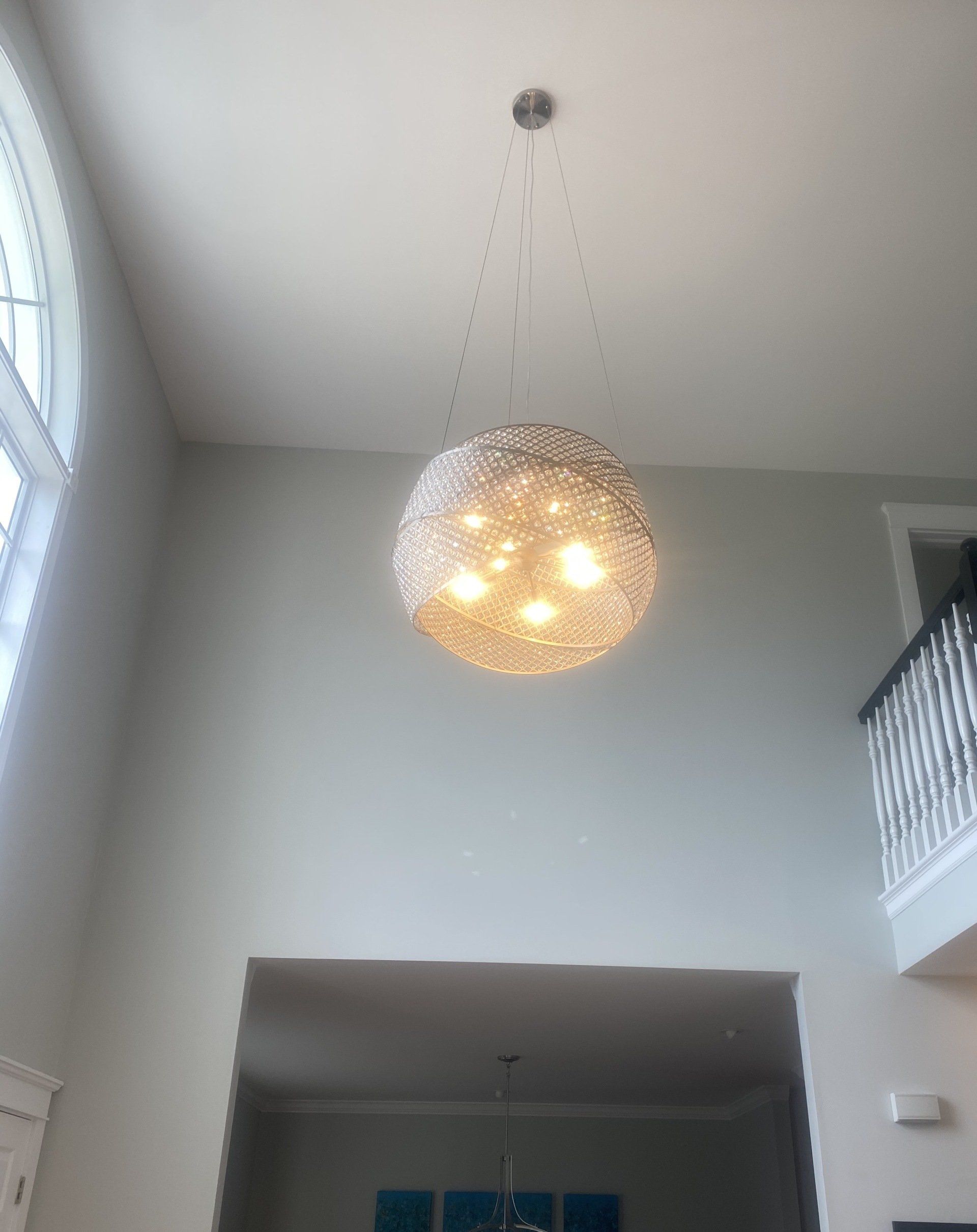 Large, round, sparkly light fixture hanging from a high ceiling. Light shines through it.